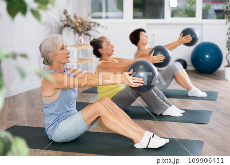 Elderly women perform softball exercises sitting on floor, workout for beautiful figure, toned body Elderly women perform softball exercises sitting on floor, workout for beautiful figure, toned body 109906431