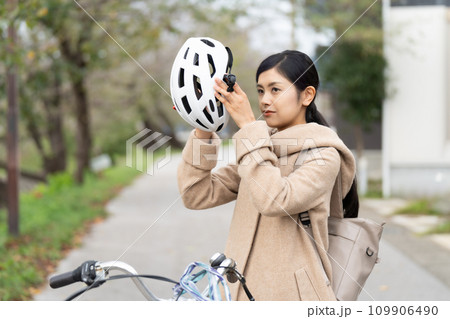 サイクリングヘルメットを被ろうとしているキャメルロングコートを着た若い女性 109906490