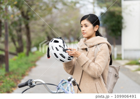 サイクリングヘルメットを被ろうとしているキャメルロングコートを着た若い女性 109906491