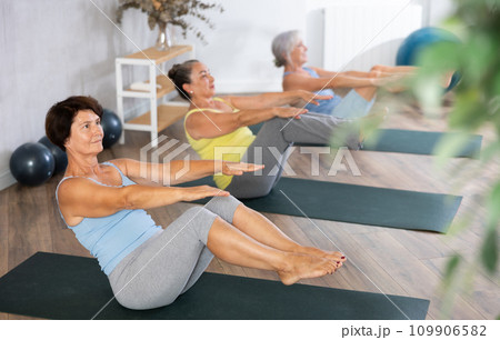 Old woman practicing boat pose of yoga in training room during fitness classes 109906582