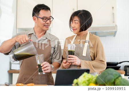 A happy Asian wife and husband are enjoying healthy green smoothie in the kitchen together A happy Asian wife and husband are enjoying healthy green smoothie in the kitchen together 109910951