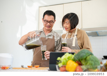 A happy Asian wife and husband are enjoying healthy green smoothie in the kitchen together A happy Asian wife and husband are enjoying healthy green smoothie in the kitchen together 109910953