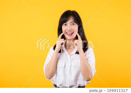 Young beautiful asian woman happy smile wearing white shirt and denim jean plants over yellow isolated background smiling confident showing and pointing with fingers teeth and mouth. Dental concept. Young beautiful asian woman happy smile wearing white shirt and denim jean plants over yellow isolated background smiling confident showing and pointing with fingers teeth and mouth. Dental concept. 109911327