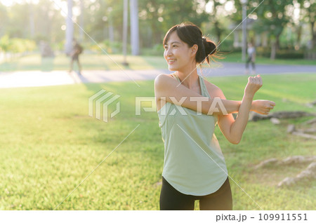 Female jogger. Fit young Asian woman with green sportswear stretching muscle in park before running and enjoying a healthy outdoor. Fitness runner girl in public park. Wellness being concept 109911551