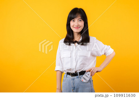 Captivating image of Asian young woman wearing white shirt and denim jeans, confidently holding cash from her shirt pocket. Fashion meets financial empowerment. Perfect for finance and fashion themes. Captivating image of Asian young woman wearing white shirt and denim jeans, confidently holding cash from her shirt pocket. Fashion meets financial empowerment. Perfect for finance and fashion themes. 109911630