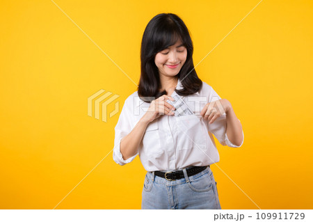 Captivating image of Asian young woman wearing white shirt and denim jeans, confidently holding cash from her shirt pocket. Fashion meets financial empowerment. Perfect for finance and fashion themes. 109911729