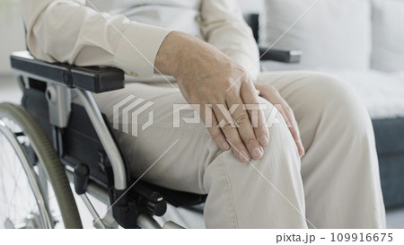 Close-up of man in wheelchair rubbing injured knee, rehabilitation after injury, arthritis 109916675