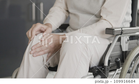 Injured man sitting in wheelchair, rubbing hurt knee, physical rehabilitation Injured man sitting in wheelchair, rubbing hurt knee, physical rehabilitation 109916684
