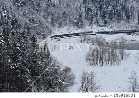 冬 信州JR飯山線千曲川沿いの雪原を走る一両編成のローカル列車（国道117号 矢垂大橋より） 109916901