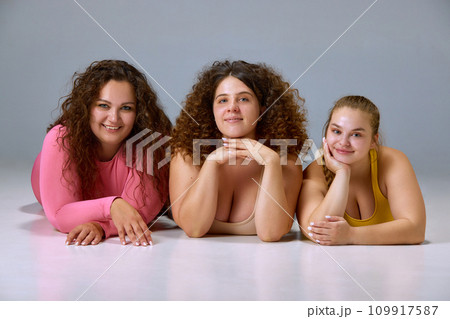 Natural beauty. Portrait of smiling young women, plus size models posing against grey studio background Natural beauty. Portrait of smiling young women, plus size models posing against grey studio background 109917587