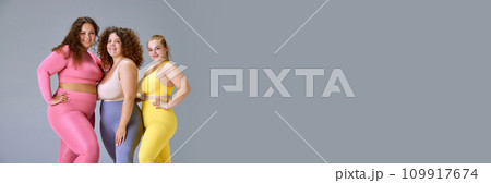 Beautiful plus size models, young women in comfortable sportswear standing against grey studio background Beautiful plus size models, young women in comfortable sportswear standing against grey studio background 109917674