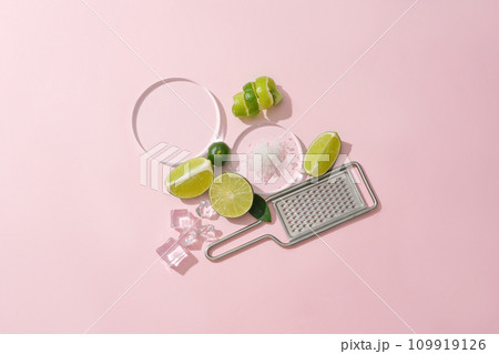 Sea salt is displayed on a glass platform, surrounded by ice and fresh lemons, a grater on a pastel pink background. Lemon is an effective skin beautifying food, treating acne and dark scars 109919126