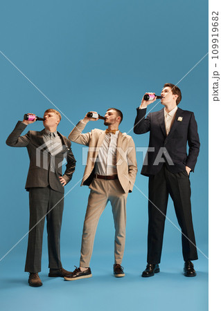 Handsome men in stylish suits, friends attending party, drinking beer against blue background. Wedding day 109919682