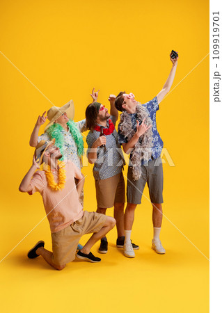 Group of cheerful friends, men in stylish clothes travelling to vacation, taking photo together against yellow background 109919701