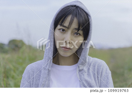 土手の小径に立つパーカー姿の若い女性の上半身のポートレート 土手の小径に立つパーカー姿の若い女性の上半身のポートレート 109919763