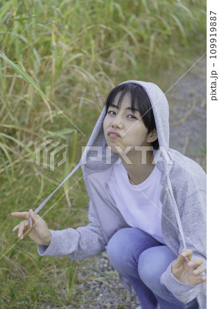 土手の小径に座ってカメラを見るパーカー姿の若い女性のポートレート 縦位置 土手の小径に座ってカメラを見るパーカー姿の若い女性のポートレート 縦位置 109919887