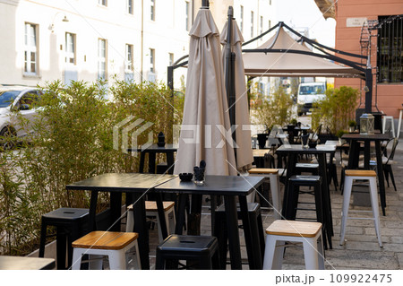 Empty chairs in outdoor cafe or restaurant on summer day. Restaurant black tables waiting for customers, old town Empty chairs in outdoor cafe or restaurant on summer day. Restaurant black tables waiting for customers, old town 109922475