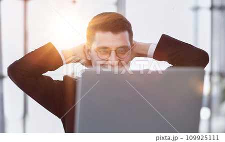 business man holding his hands behind his head while working on a laptop 109925111