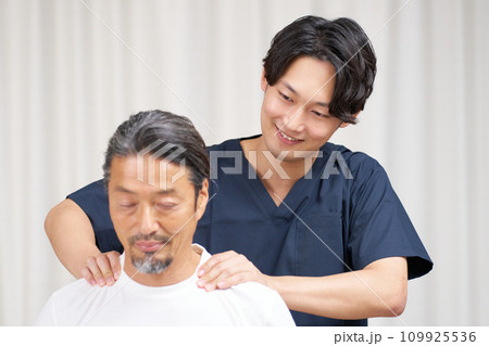 高齢男性にマッサージを行う若い整体師 109925536