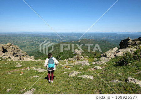 A woman with a backpack travels in the mountains. Beautiful panoramic view of the mountains covered with forest. Summer day 109926577