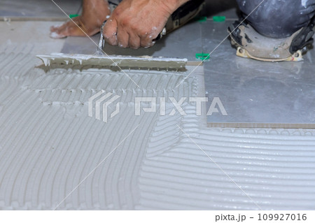 Tiler applying adhesive mortar cement plaster surface to floor for lays ceramic tile Tiler applying adhesive mortar cement plaster surface to floor for lays ceramic tile 109927016