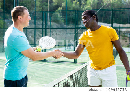 Two men shake hands after playing padel on outdoor tennis court Two men shake hands after playing padel on outdoor tennis court 109932758