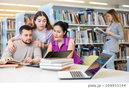 Three adult students work on laptop and read books in a public library 109933144