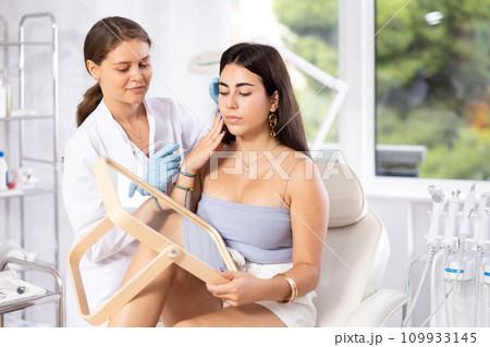 Aesthetician giving professional advice before facial skin treatments to young brunette Aesthetician giving professional advice before facial skin treatments to young brunette 109933145