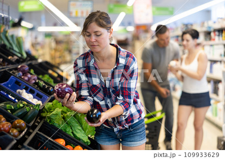 Woman choosing eggplants in fruit and vegetable section of supermarket 109933629