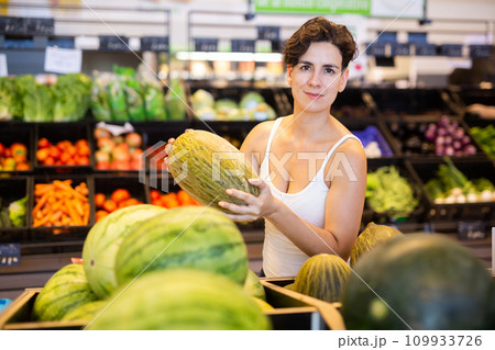 Young Hispanic woman choosing ripe melon in supermarket Young Hispanic woman choosing ripe melon in supermarket 109933726