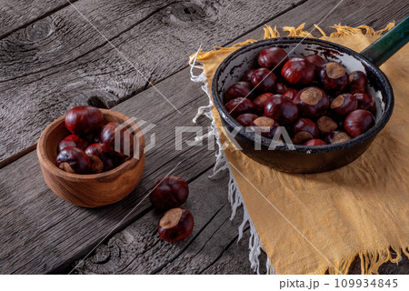 Chestnut in Frying Pan and Wooden Plate on Wooden Background. Chestnut in Frying Pan and Wooden Plate on Wooden Background. 109934845