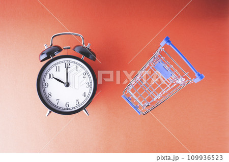 An empty shopping cart and an alarm clock on a red scarlet background. Shopping, online shopping concept, time to buy concept, copy space, top view, An empty shopping cart and an alarm clock on a red scarlet background. Shopping, online shopping concept, time to buy concept, copy space, top view, 109936523