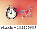An empty shopping cart and an alarm clock on a red scarlet background. Shopping, online shopping concept, time to buy concept, copy space, top view, 109936605