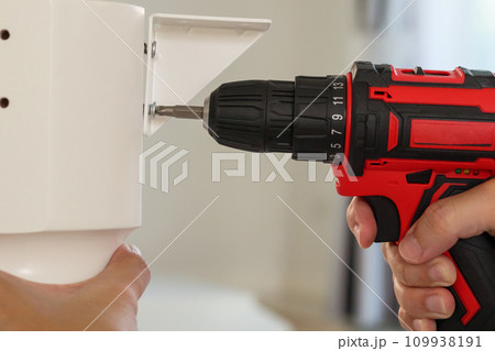 man assembling white table furniture at home using cordless screwdriver 109938191