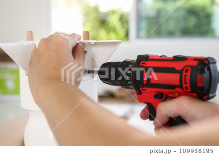 man assembling white table furniture at home using cordless screwdriver man assembling white table furniture at home using cordless screwdriver 109938195