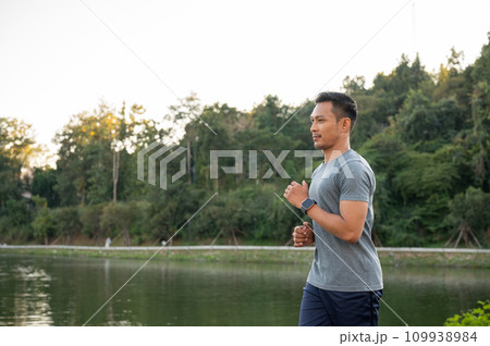 A handsome, focused Asian man in sportswear is running outdoors in the morning. A handsome, focused Asian man in sportswear is running outdoors in the morning. 109938984