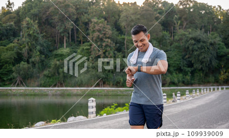 A healthy Asian man in sportswear is his calories burning on his smartwatch while running outdoors. A healthy Asian man in sportswear is his calories burning on his smartwatch while running outdoors. 109939009