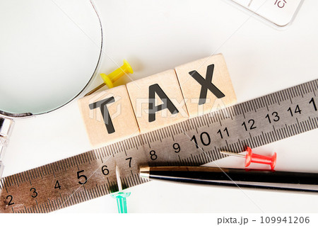 TAX text of non-wooden cubes next to a calculator, pen, measuring ruler, magnifying glass on a white background TAX text of non-wooden cubes next to a calculator, pen, measuring ruler, magnifying glass on a white background 109941206