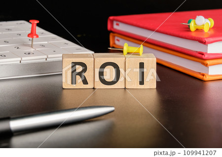 Return on investment concept. ROI the text of non-wooden cubes next to notepads, a calculator, a pen on a black background Return on investment concept. ROI the text of non-wooden cubes next to notepads, a calculator, a pen on a black background 109941207