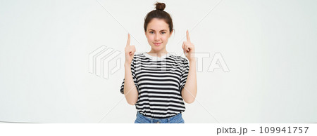 Lifestyle and advertisement concept. Young smiling woman, modern girl, pointing finger at promo, showing banner, place with text, isolated on white background Lifestyle and advertisement concept. Young smiling woman, modern girl, pointing finger at promo, showing banner, place with text, isolated on white background 109941757