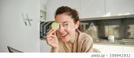 Portrait of happy, smiling young woman in the kitchen, cooking, chopping zucchini, holding vegetables and looking happy, preparing vegan food meal at home 109942932