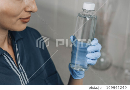 Woman scientist holding bottle with transparent liquid in her hands in chemical laboratory background, science laboratory research and development concept 109945249