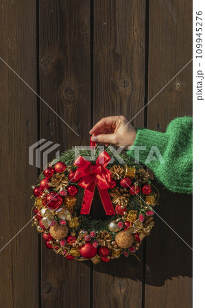 Womans hand in green sweater hanging up fir wreath for advent. Christmas Eve and Decorating. New Year celebration. 109945276