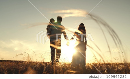 Silhouettes of parents walk holding hands with daughter sitting in arms of father 109945282