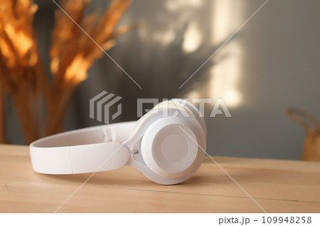 White headphones on wooden table and bouquet of dry flowers over gray house wall with sunlight shadows copy space advertisement area 109948258