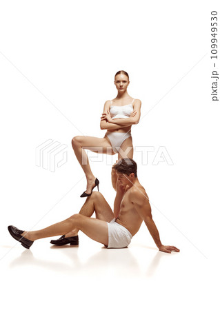 Full length portrait of beautiful couple, man sitting on floor and woman stands under him and put her leg on males knee against white background. Full length portrait of beautiful couple, man sitting on floor and woman stands under him and put her leg on males knee against white background. 109949530