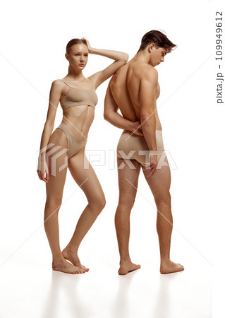 Body size portrait of naked couple, woman and man with perfect athletic bodies posing in beige underwear against white studio background. Body size portrait of naked couple, woman and man with perfect athletic bodies posing in beige underwear against white studio background. 109949612