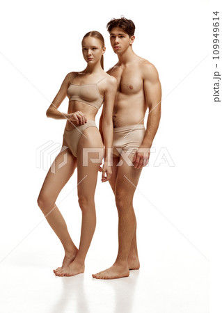 body size portrait of attractive beloved couple with perfect body shapes posing in beige underwear against white studio background. body size portrait of attractive beloved couple with perfect body shapes posing in beige underwear against white studio background. 109949614