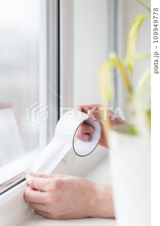 Mans hands putting draught excluder tape on the window. Mans hands putting draught excluder tape on the window. 109949778