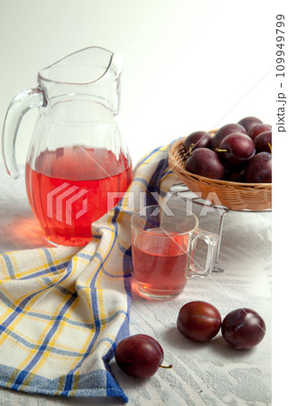 Plum Compote in jug with purple plums on white wooden background. . Plum Compote in jug with purple plums on white wooden background. . 109949799